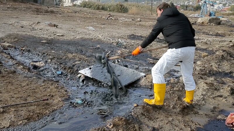 Der Künstler (Michael Hirschbichler) mit gelben Gummistiefeln in einer Ölpfütze schaufelt öliges Wasser auf eine Leinwand. – Bild: ORF/NAVIGATOR FILM & Vive LaDok Der Künstler (Michael Hirschbichler) mit gelben Gummistiefeln in einer Ölpfütze schaufelt öliges Wasser auf eine Leinwand. – Bild: ORF/NAVIGATOR FILM & Vive LaDok