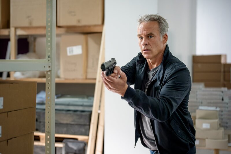 Jan Maybach (Marco Girnth) steht mit gezogener Waffe in einem Lagerraum – er glaubt weiterhin an Rico Schäfers Unschuld. – Bild: Uwe Frauendorf /​ ZDF