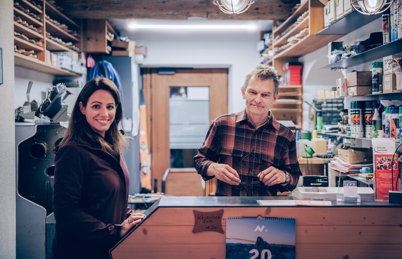 Lisa Gadenstätter wird im Sportgeschäft von Georg Überall mit Steigeisen für die eisige Streif ausgestattet. – Bild: Neulandfilm /​ ORF /​ Benny Paya