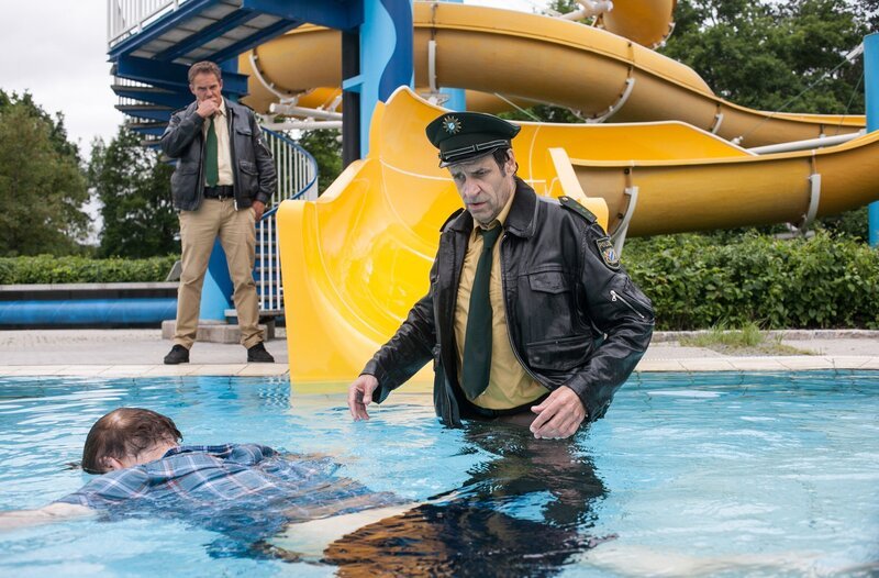 Hubert (Christian Tramitz, links) und Staller (Helmfried von Lüttichau, rechts), machen im Schwimmbad einen grausigen Fund. Auf der Wasserrutsche sitzt Bademeister Frank Brauß, erstochen! Bei dem Versuch den Toten genauer zu betrachten, rutscht Staller samt der Leiche ins Wasser. – Bild: ARD/​TMG/​Arvid Uhlig