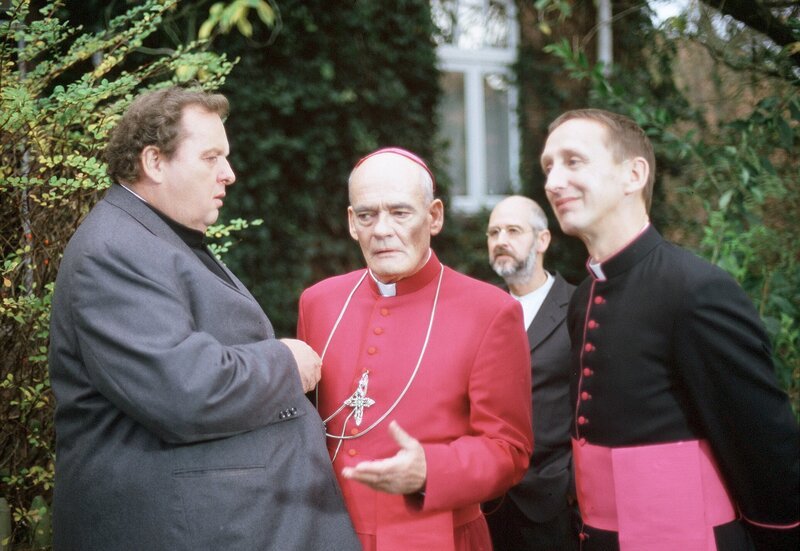 Pfarrer Brauns (Ottfried Fischer, li.) Beliebtheit bei seinem Vorgesetzten, Bischof Hemmelrath (Hans-Michael Rehberg, Mitte) und dessen Sekretär Mühlich (Gilbert von Sohlern, re.) scheint trotz hoher Verbrechensaufklärungsquote nicht zu steigen. – Bild: HR/​ARD/​Degeto/​Romano Ruhnau