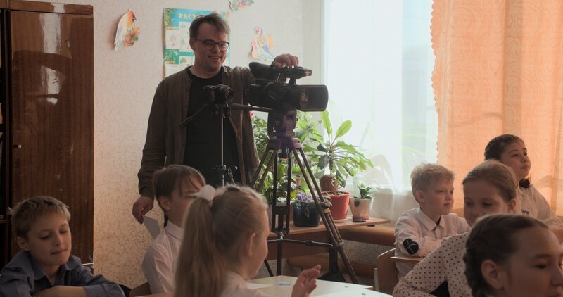Pawel „Pascha“ Talankin mit seiner Videokamera in einem Klassenzimmer. – Bild: Loco Films