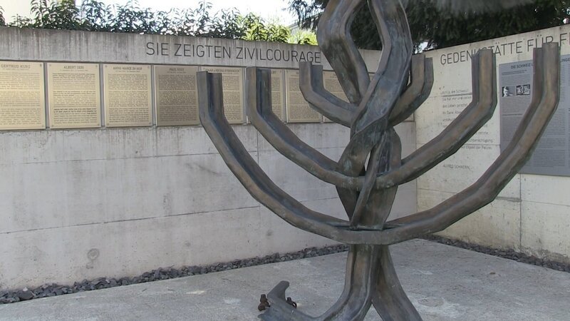 Eine Menora aus Eisenbahngleisen in Erinnerung an die Deportationszüge, im Hintergrund Tafeln zu Ehren von Judenrettern in der Schweiz. – Bild: 3sat