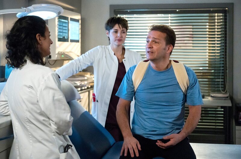 Peer Nürtinger (Mathias Hermann, r.) wird von Leyla (Sanam Afrashteh, l.) und Theresa (Katharina Nesytowa, M.) im Behandlungsraum untersucht. Er klagt über Schmerzen in der Schulter. – Bild: ARD/​Jens Ulrich Koch