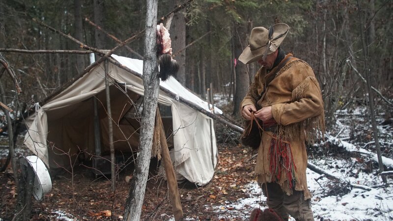 Oliver tying his coat, standing outside wall tent. – Bild: Discovery Communications, LLC