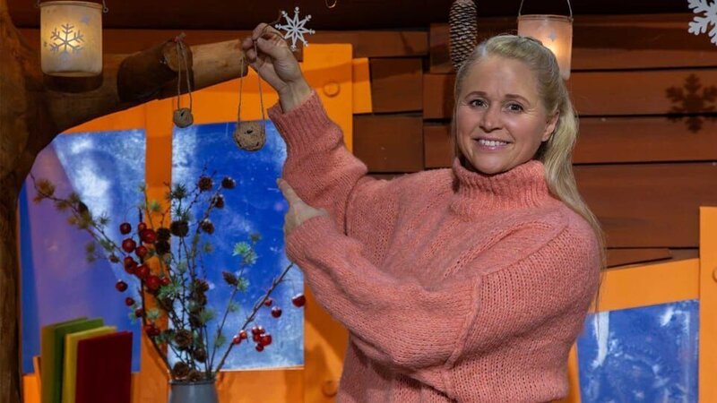 Singa zeigt einen Meisenknödel von dem bereits einige Vögel gegessen haben und will weitere aufhängen. – Bild: KiKA