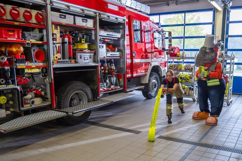 TanzTapir schaut zu, wie der Feuerwehrschlauch ausgerollt wird. – Bild: KiKA/​MingaMedia/​Ron Bergmann