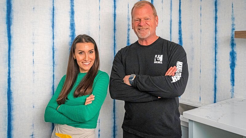 Mike (left) and Katie (right) pose in front of the freshly installed wallpaper in Kim and Sandor’s laundry room. – Bild: HGTV US /​ Restovate Ltd. /​ Discovery, Inc.