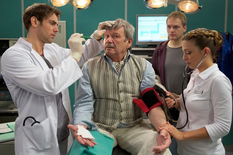 Der Weinhändler Edmund Dannenberg (Wolfgang Winkler, Mitte) wird mit einer starken Migräneattacke in die Sachsenklinik eingeliefert. Sein Sohn Björn (Knud Riepen, hinten) begleitet ihn. Da Dr. Niklas Ahrend (Roy Peter Link, links) keine Ursache finden kann, bittet er Schwester Arzu (Arzu Bazman) ihm ein Zimmer vorzubereiten und einen Termin für ein MRT zu machen. Edmund Dannenberg passt es gar nicht, länger in der Klinik zu bleiben – so muss sein Weinladen geschlossen bleiben. Als sein Sohn Björn ihm anbietet, er könne doch den Laden öffnen, lehnt Edmund dies vehement ab. – Bild: MDR/​Tom Schulze