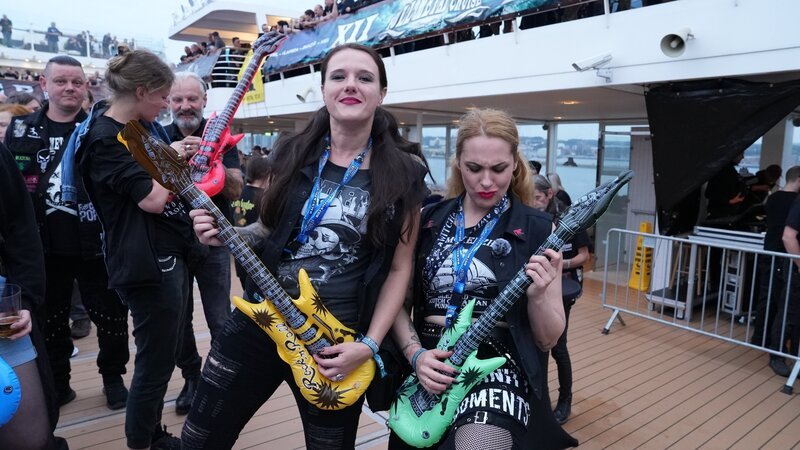 Heavy Metal-Fans Vanessa Wüpping (l.) und Birte McNeely (r.) posieren mit aufblasbaren Gitarren an Deck. – Bild: ZDF und Thiemo Hackenberg