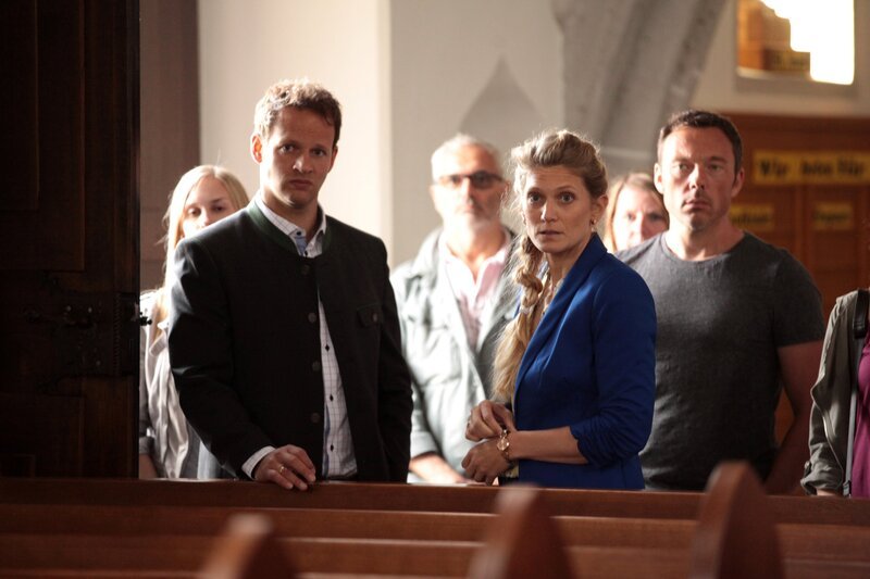 Martin Kleeberg und seine Frau Ingrid wundern sich über die Schüsse vor der Kirche, die Pfarrer Uli Wagner galten. (vorne v.l.n.r.: Martin Kleeberg (David Miesmer), Ingrid Kleeberg (Magdalena Kronschläger, hinten: Komparsen)). „SOKO Wien – Die Todesliste“: Die Dorfbewohner sind erschrocken darüber, was vorgefallen ist. Fotograf: Stefan Haring – Bild: Bavaria Media GmbH /​ ZDF /​ Stefan Haring