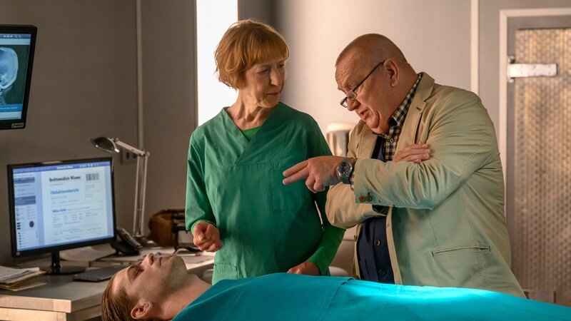 Rechtsmedizinerin Dr. Helene Sturbeck (Katharina Blaschke, M.) hat die Obduktion der Leiche von Niklas Keller (Komparse, l.) abgeschlossen und teilt Revierchef Jan-Hinrich Reuter (Udo Kroschwald, r.) ihre Erkenntnisse mit. Todesursache war ein Schädelbasisbruch durch Aufprall auf eine Tischkante. Der Schlag mit dem Anzapfschlegel allein war nicht tödlich. Wer hatte ein Motiv, den Stadtrallye-Organisator zu töten? – Bild: ZDF und Marc Meyerbröker