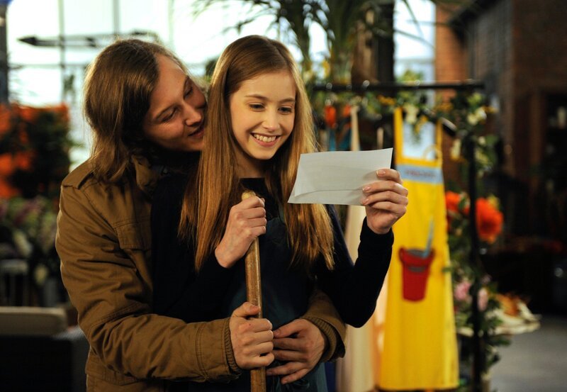 Brian (Alexander Becht, l.) überrascht Lotte (Anna Willecke, r.) mit Flugtickets nach England. – Bild: ARD/​Nicole Manthey