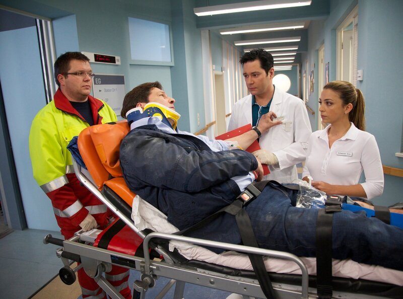 Christoph Maler (Francis Fulton Smith, liegend) hat sich bei dem Unfall das Bein gebrochen. Als er vom Notarzt (Komparse, links) eingeliefert wird, will er nur eins wissen: Wie geht es seiner Tochter? Sein behandelnder Arzt Dr. Philipp Brentano (Thomas Koch, 2. von rechts) und Schwester Arzu (Arzu Bazman) dürfen und können ihm dazu noch keine Auskunft geben. – Bild: MDR/​Wernicke