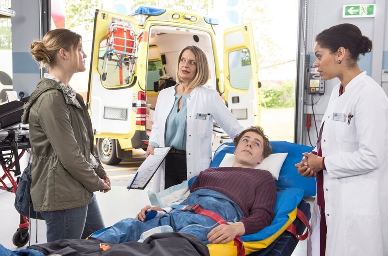 Tino Grein (Julian Gutmann, 2.v.r.) wird mit einem gebrochenen Arm ins JTK gebracht – mit dabei seine Ehefrau Maren (Nele Trebs, l.). Dr. Franziska Ruhland (Gunda Ebert, 2.v.l.) und Vivienne Kling (Jane Chirwa, r.) nehmen die beiden in der Notaufnahme in Empfang. – Bild: ARD/​Jens Ulrich Koch