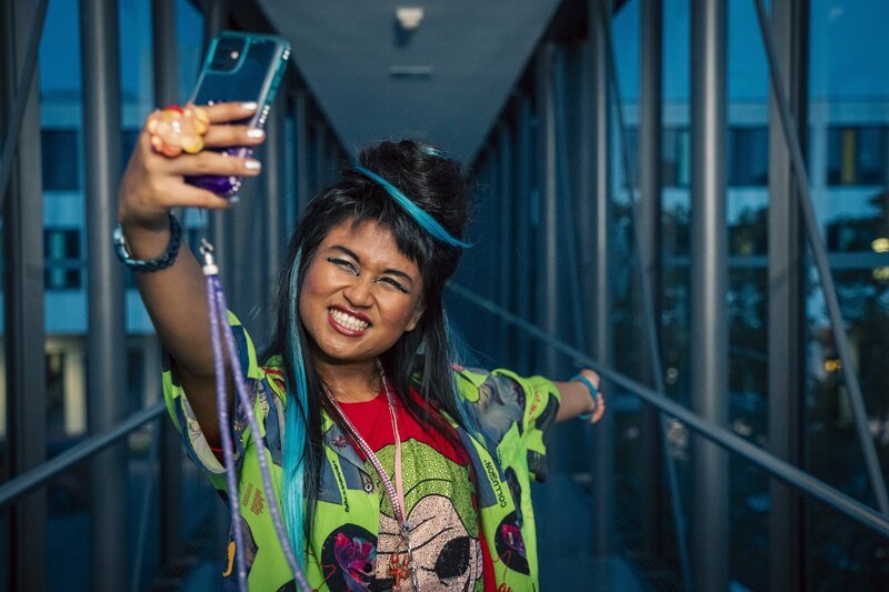 Massuda (Tisa Pharischad Khumyim) stellt sich vor, wie sie live von der BeautyCon in Amsterdam berichtet. – Bild: mdr/​Saxonia Media/​Thomas Dietze