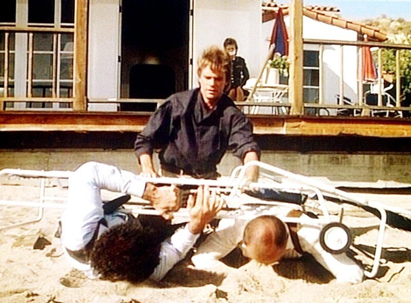 Mit Hilfe einer Krankenhaustrage hat MacGyver (Richard Dean Anderson, M.) zwei Verbrecher überwältigt, die einen weiblichen Offizier (hinten) in ihrer Gewalt hatten. – Bild: Kabel Eins Classics