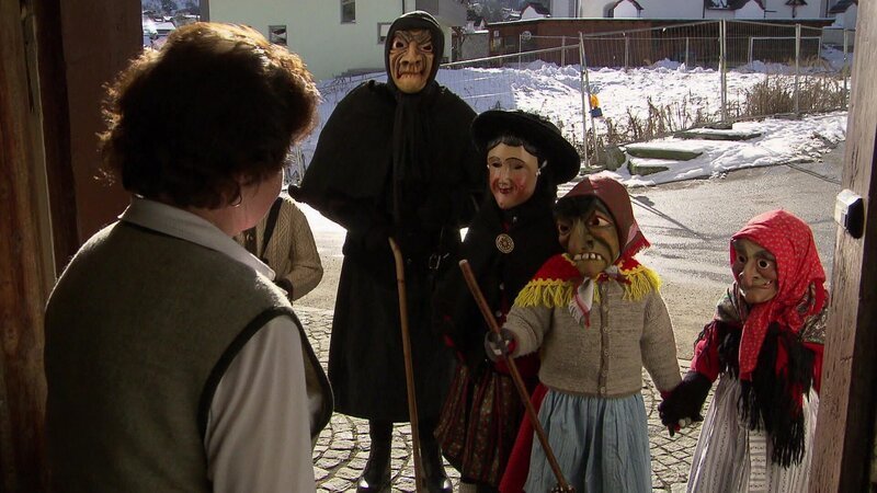 Eine Gruppe von Menschen in traditionellen Kostümen steht an einer Haustür im Winter. – Bild: @Red Bull Media House/​ServusTV