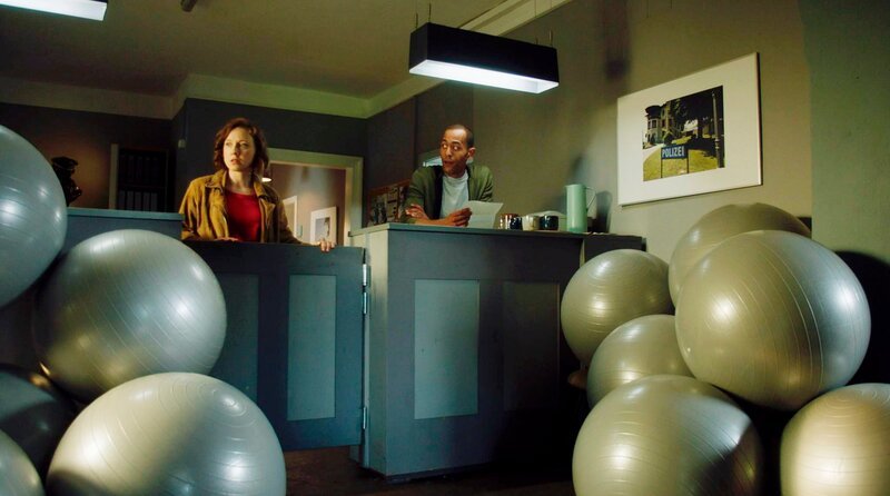 Zwischen Gymnastikbällen und Bürokaffee rätseln Sophia Strasser (Katharina Leonore Goebel, l.) und Jerry Paulsen (Peter Marton, r.), wer für diese Lieferung verantwortlich ist. – Bild: ARD/​Lucky Bird Pictures/​Luis Koppelkamm