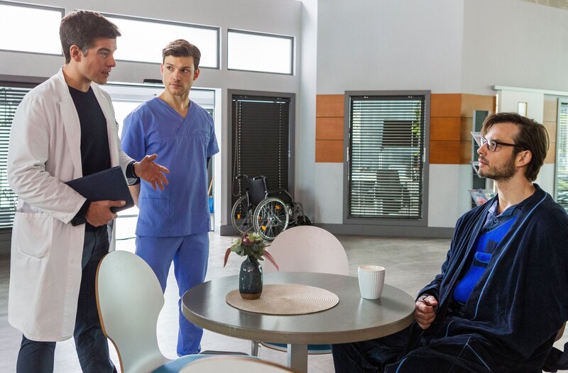 Dr. Ben Ahlbeck (Philipp Danne, l.) und Florian Osterwald (Lion Wasczyk, 2.v.l.) klären den Patienten Ludger Holm  (Marc Schöttner, r.) über seine besondere Diagnose auf. – Bild: ARD/​Tom Fülle