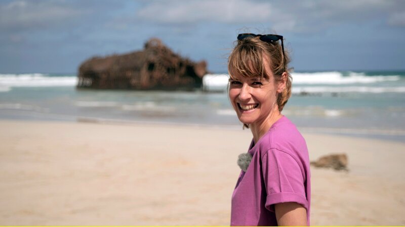 Nina Heins besucht das Schiffswrack der Cabo Santa Maria (Im Hintergrund links). 1968 lief das spanische Frachtschiff Cabo Santa Maria vor der Küste der Kapverden-Insel Boa Vista auf Grund. – Bild: ZDF und HR/​Jonas Weinhold