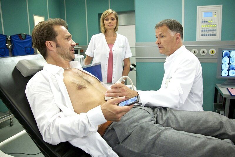 MDR Fernsehen IN ALLER FREUNDSCHAFT FOLGE 625, „Kontroversen“. Olaf Beck (Mathias Herrmann, li.), Bauunternehmer, wird mit starken Schmerzen von einem seiner Mitarbeiter in die Sachsenklinik eingeliefert. Als Dr. Roland Heilmann (Thomas Rühmann, re.) ihn mit Hilfe von Schwester Yvonne (Maren Gilzer, mi.) untersucht, wird eine vergrößerte Leber festgestellt. Dr. Heilmann glaubt zunächst an Alkoholmissbrauch. Olaf bestreitet das jedoch vehement. Schwester Yvonne findet Olaf Beck sofort attraktiv, seine selbstgefällige Art nervt sie jedoch schon bei der Untersuchung. Nachdem er immer wieder Telefonate während der Behandlung führt, nimmt sie ihm resolut das Handy aus der Hand. – Bild: MDR/​Saxonia/​Wernicke