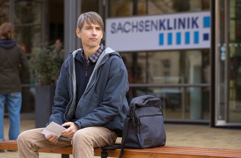 Mirko Hoffmann (Axel Schreiber) wartet auf vor der Sachsenklinik auf seinen Bruder Dr. Kai Hoffmann, um ihm einen Brief ihrer verstorbenen Mutter zu geben. – Bild: MDR/​Rudolf Wernicke