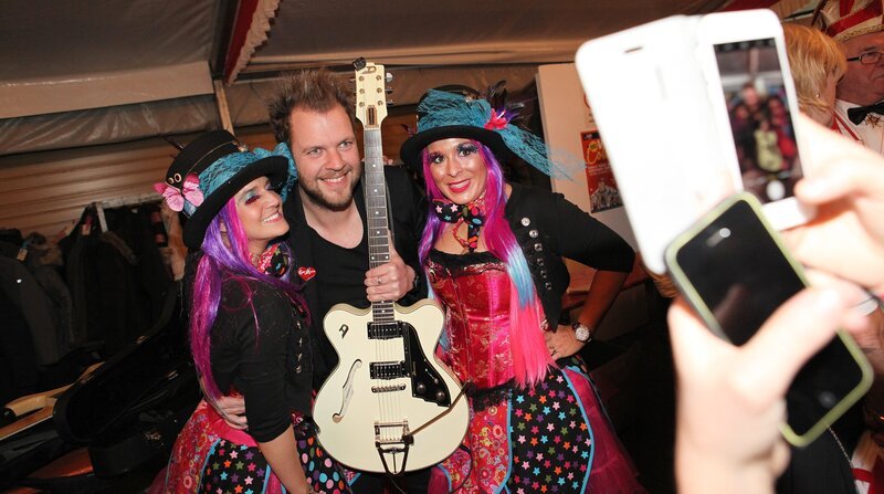 Vettweiß – hier lebt er, der echte, ehrliche und ursprüngliche Karneval auf dem Dorf. In jedem Jahr organisiert und feiert die Dorfgemeinschaft die „Hölle von Vettweiß“. Aus dem Örtchen wird eine jecke Party-Metropole. Über 10.000 Besucher innerhalb einer Woche. Ein Hauch von Wacken – dem Heavy-Metal-Mekka in Norddeutschland – weht dann in dem Dorf in der Voreifel. Am beliebtesten sind die Damensitzungen. Rund 2.000 Besucherinnen strömen täglich in das Festzelt auf dem Schulhof. Sie kommen nicht nur aus der Umgebung, sondern mittlerweile auch aus Belgien, dem Ruhrgebiet sowie Nord- und Süddeutschland. Das gebotene Programm ist hochkarätig: Brings, Kasalla, Paveier, Klüngelköpp, Räuber, Marita Köllner, Höhner, aber auch Büttenredner wie Martin Schopps, treten auf und begeistern die Damen. – Sven Welter von der Band „Paveier“ umringt von seinen weiblichen Fans. – Bild: WDR/​Sibylle Anneck