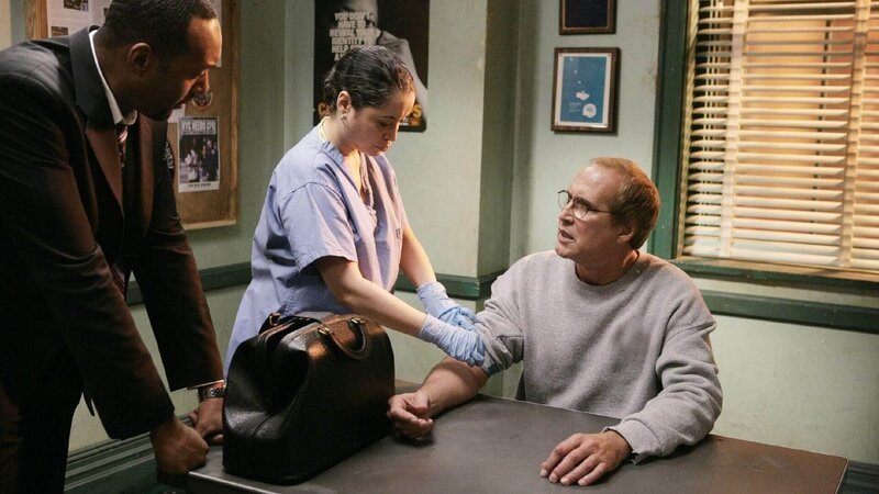 Der arbeitslose Schauspieler Mitch Carroll (Chevy Chase, re.) wird betrunken und mit blutbefleckter Kleidung während einer Verkehrskontrolle verhaftet. Während ihm eine Schwester (Susanna Guzman) Blut abnimmt, wird er von Det. Green (Jesse L. Martin) befragt. – Bild: RTL Deutschland