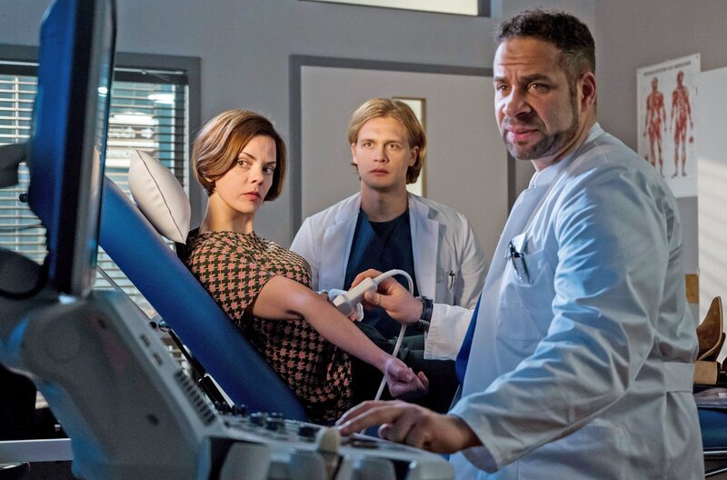 Während der Untersuchung von Ramona Zergiebel (Camilla Renschke, l.) wetteifern die beiden Ärzte Mikko Rantala (Luan Gummich, M.) und Matteo Moreau (Mike Adler, r.) – Bild: ARD/​Jens Ulrich Koch