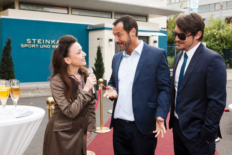 Simone (Tatjana Clasing) und Richard (Silvan-Pierre Leirich, M.) freuen sich, den Stardesigner Luigi Sabatoni (Marcel ‚Mars‘ Saibert) bei der Neueröffnung des Zentrums begrüßen zu können. – Bild: RTL Passion