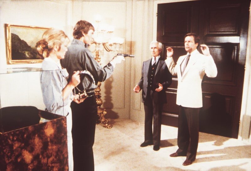 Monique (Monique Renoir, l.) und Tommy (Michael Halsey, 2.v.l.) nehmen Claude (Roger Til, 2.v.r.) und Jonathan (Robert Wagner) als Geiseln. Sie wollen so freien Abzug aus der Galerie erzwingen. Haben sie mit dieser Methode Erfolg? – Bild: Sat.1 Gold