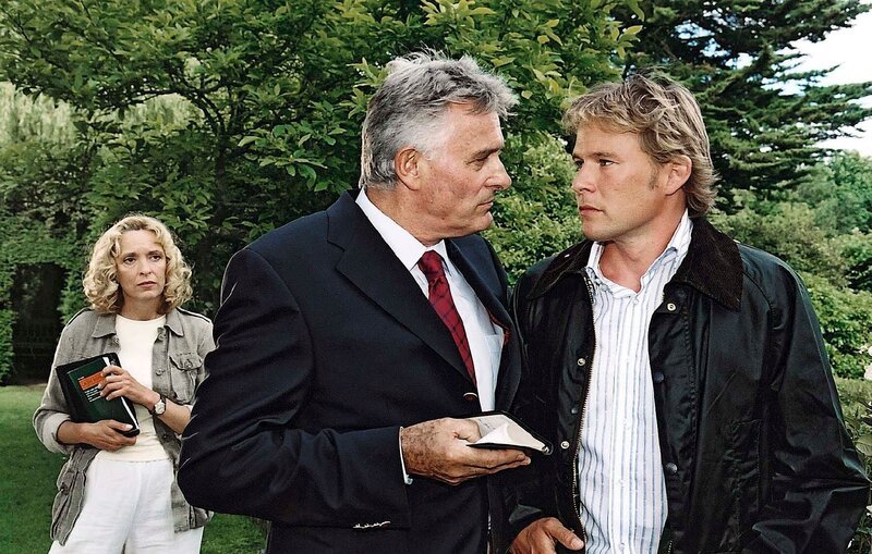 Hugh Hanthorpe (Klaus Wildbolz) bittet Julian (Oliver Clemens), nach Neuseeland zu reisen, um sich dort um sein durch ein schweres Unwetter verwüstetes Anwesen zu kümmern. Das ist allerdings nicht der einzige Grund, weshalb Hugh Julian ein wenig von der Bildfläche haben will. – Bild: DMB