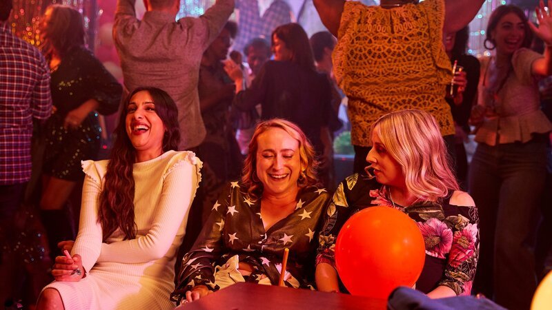Die Party ist ein voller Erfolg. Während die anderen auf der Tanzfläche feiern, sitzen Rana (Taj Atwal, l.), Toni (Leah Brotherhead, M.) und Paula (Sinead Matthews, r.) zusammen und genießen die ausgelassene Stimmung. – Bild: ZDF und Amy Brammall