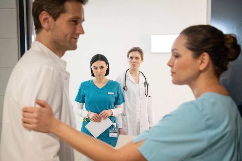 Dr. Sebastian Sander (Oliver Franck) berichtet Ella (Ines Quermann, r.) von seinem schwer kranken Freund. Nora (Mimi Fiedler, 2.v.l.) und Dr. Claudia Cramer (Isabel Bergout, 2.v.r.) beobachten die Vertrautheit zwischen Ella und dem Arzt. – Bild: TVNOW /​ Christoph Assmann