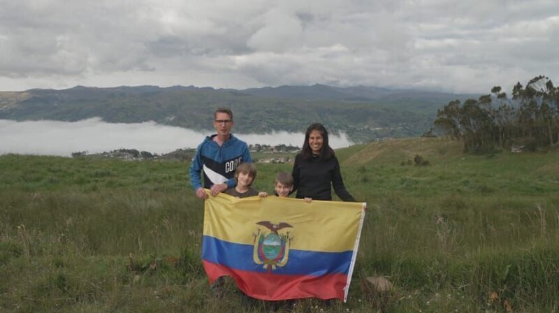 Eine Familie steht auf einer grasigen Wiese und hält die ecuadorianische Flagge vor einer Berglandschaft. – Bild: CH Media