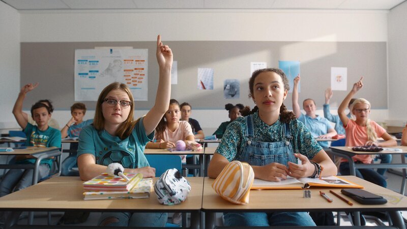 Floor (Bobbi Mulder) und Margreet (Romy Voll) sitzen im Klassenzimmer, Floor meldet sich, als der Lehrer fragt, wer dem Schachclub beitreten will. – Bild: NDR/​NL Film