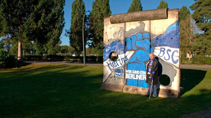 Ein glühender Hertha-Fan, ein leidenschaftlicher Anhänger der DFB-Elf und Bürger der DDR: Helmut Klopfleisch reiste nach dem Bau der Mauer seinen Lieblingsmannschaften hinterher – und geriet so ins Visier der Stasi. – Helmut Klopfleisch vor der „Hertha-Wand“. – Bild: rbb/​Hans-Jürgen Büsch