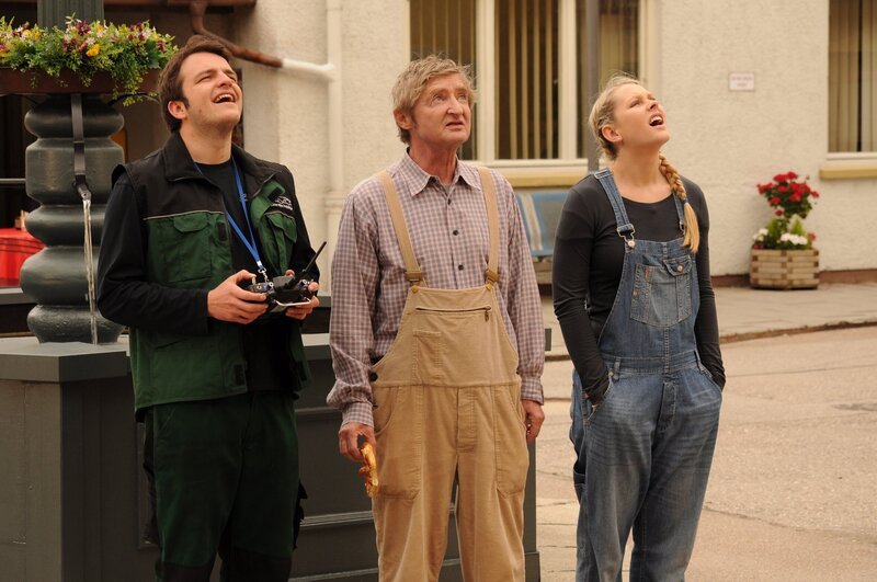 Xaver und Yvi beobachten, wie Flori den Heli Richtung Dachrinne lenkt. Von links: Florian Brunner (Tommy Schwimmer), Xaver (Michael Schreiner) und Yvonne Preissinger (Alexa Eilers). – Bild: BR/​Jo Bischoff