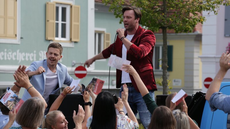 Pedro Pilzner (Wolfgang Cerny, r.) und sein Agent Leo Lindner (Ferdinand Hofer, l.) beim Auftritt auf dem Marktplatz in Pöllau. (Komparsen im Bild). – Bild: ZDF und SATELFILM/​stefanharing