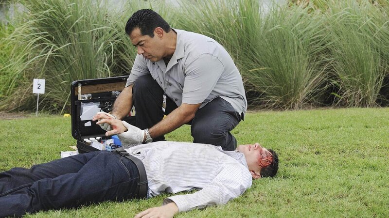 Carlos (Carlos Gomez) untersucht die Leiche des ehemaligen Caddys Douglas Packard (Ford D’Aprix, lieg.), der kurz nach der Entlassung aus dem Gefängnis erschlagen auf einem exklusiven Golfplatz aufgefunden wurde. – Bild: TVNOW