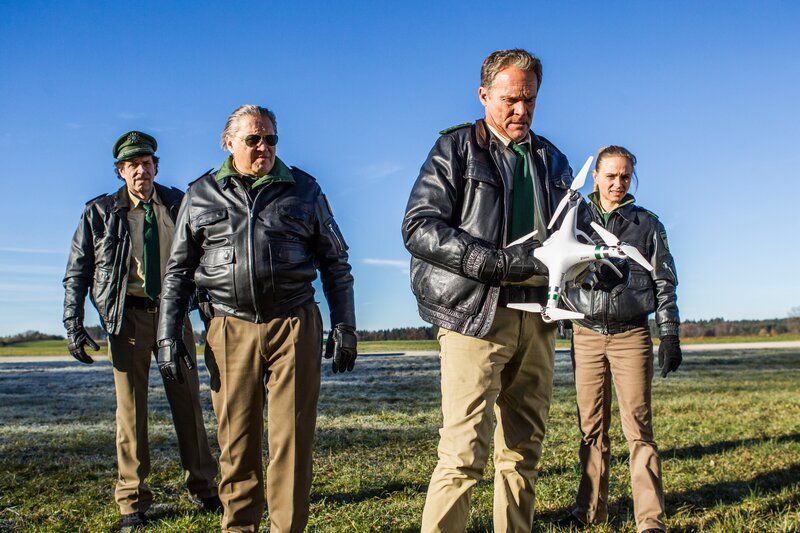 Mehrere Anzeigen sind im Revier eingegangen. Aufgebrachte Anruferinnen melden Belästigungen durch eine Drohne. Hubert (Christian Tramitz, 2. von rechts), Staller (Helmfried von Lüttichau, links), Girwidz (Michael Brandner, 2. von links) und Sonja (Annett Fleischer) wollen wissen, wer die Drohne steuert. – Bild: Leonine /​ Chris Hirschhäuser