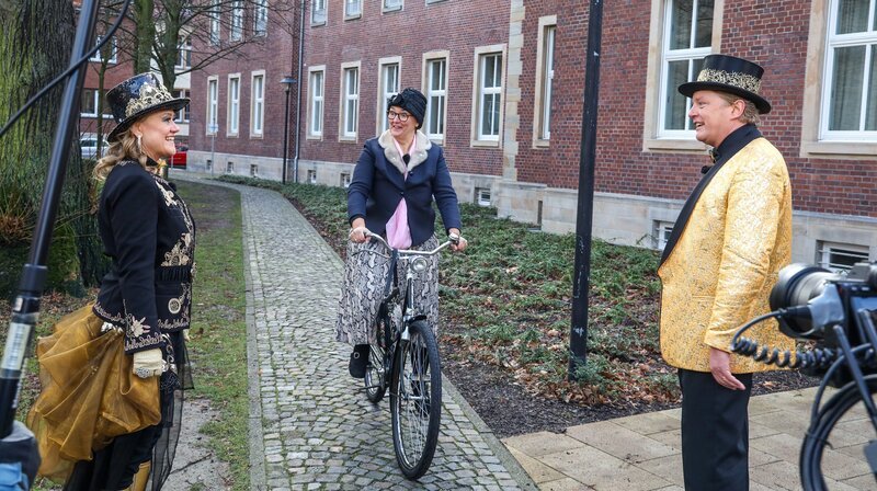 Comedy-Queen Lisa Feller (r) und der langjährige Sitzungsmoderator Uwe Koch (l) führen durch diese ganz besondere karnevalistische Rankingshow und stellen die 50 besten Momente vor, die vom Redaktionsteam ausgewählt wurden. Münsters wunderschöne Innenstadt mit seinen historischen Bauten und Plätzen ist die Kulisse, vor deren Hintergrund das Moderatoren-Duo die einzelnen Platzierungen präsentiert. Entlang des Weges gibt es witzige Begegnungen mit närrischen Akteur*innen aus dem westfälischen Karneval. – Lisa Feller (r) und Uwe Koch (l) treffen in Münster auf die beliebte Büttenrednerin „Hertha“. – Bild: WDR/​Rüdiger Wölk