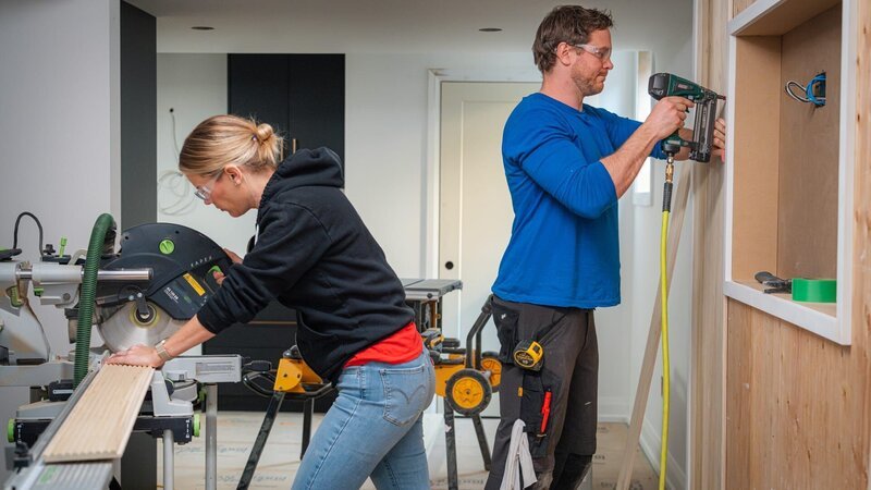 Sherry Holmes (left) uses a chop saw to cut dowel board to length as Michael Holmes (right) tacks it to the wall with a brad nailer as seen on HGTV’s Holmes Family Rescue Season 2 Episode 14. – Bild: Warner Bros. Discovery, Inc. or its subsidiaries and affiliates. All rights reserved.