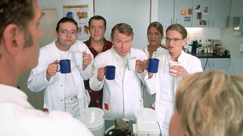 Die Assistensärzte (hinten v.l. Alexander Schottky, Oliver Reinhard, Roland Jankowsky, Nancy Geisler, Kerstin Thielemann) schmeicheln sich bei Dr. Schmidt (Walter Sittler, l.) und Nikola (Mariele Millowitsch, r.) ein: Wer kocht den besten Kaffee? – Bild: RTL /​ Guido Engels
