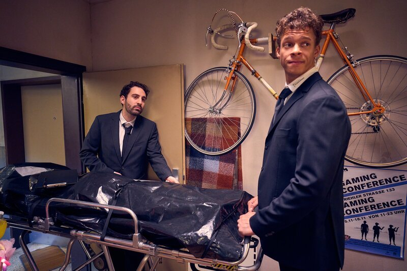 Zwei Bestatter (v. l.: Fabian Rommel, Malcolm Quinnten Henry) tauchen in der Wohnung von Caro und Yannik auf. – Bild: Frank Dicks /​ ZDF