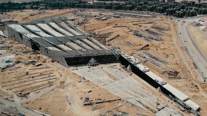 Blick von oben auf die riesige Baustelle des Grand Egyptian Museums mit der Stadt Kairo im Hintergrund. – Bild: BR