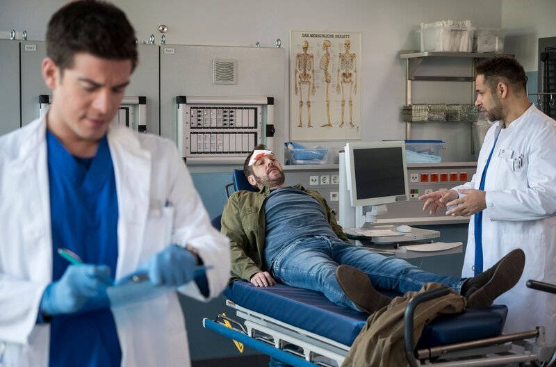 Nach einem Treppensturz kommt Axel Becker (Jens Kipper, M.) in die Notaufnahme. Matteo (Mike Adler, r.) und Ben  (Philipp Danne, l.) hatten den Patienten für eine Nierentransplantation vorgesehen. Doch durch den Sturz verschiebt sich der ganze Zeitplan. – Bild: ARD/​Jens Ulrich Koch