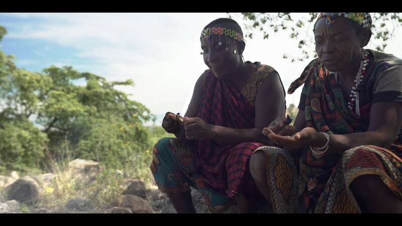Two hadzabe enjoying a meal by the fire. – Bild: Rollercoaster Road Productions 2018
