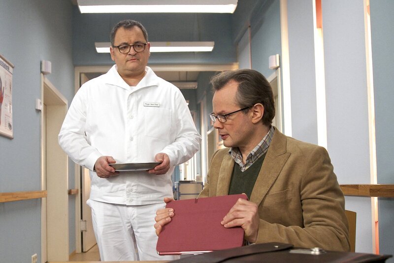 Pfleger Hans-Peter Brenner (Michael Trischan, links) ertappt Lenas Vater Frank Arnold (Marco Hofschneider) dabei, als er sich ein Fernsehinterview mit Lenas Mutter anschaut. Frank hat seiner Tochter gesagt, dass sie gestorben sei und streitet ab, dass es sich bei der Frau im Fernsehen um Lenas Mutter handelt. Brenner kann ihm das nicht glauben. – Bild: MDR/​Saxonia/​Wernicke